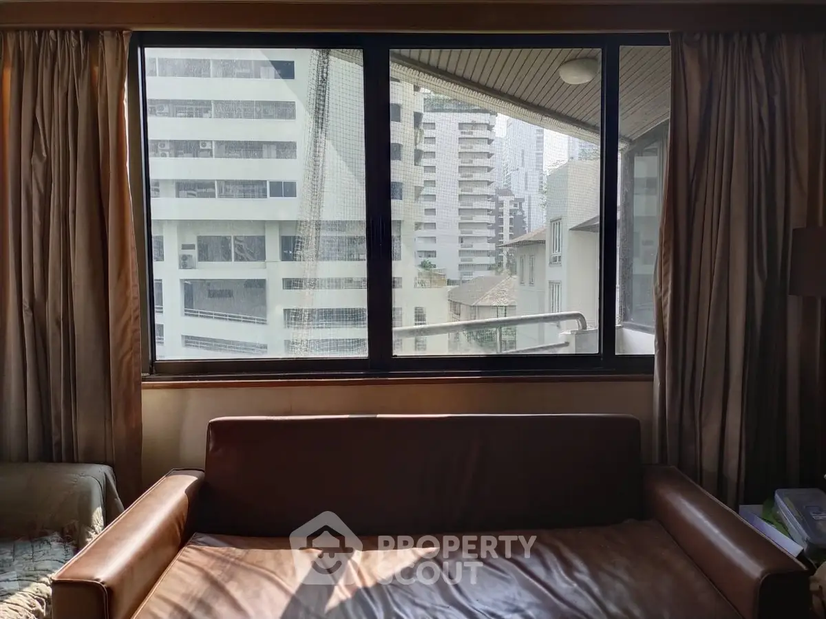 Cozy living room with city view through large window, featuring a comfortable leather sofa and elegant curtains.
