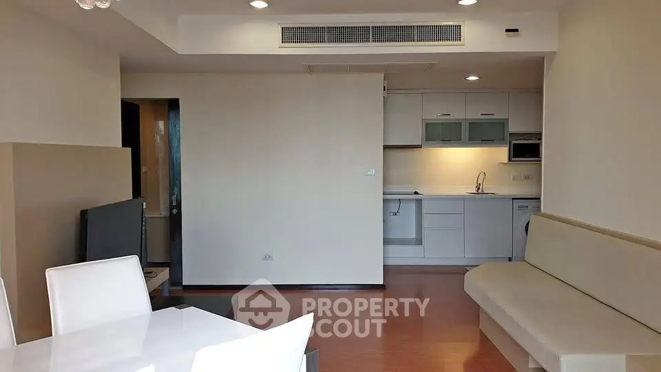 Modern open-plan living room with sleek kitchen and dining area, featuring contemporary furniture and lighting.