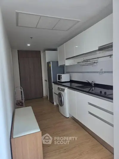 Modern kitchen with sleek cabinetry, washing machine, and microwave in a compact layout.