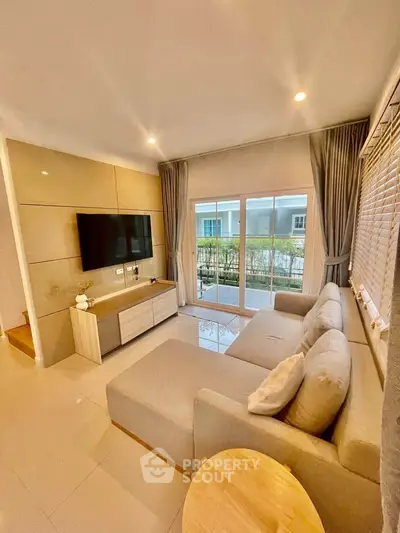 Modern living room with large sofa and TV, overlooking a balcony with garden view.