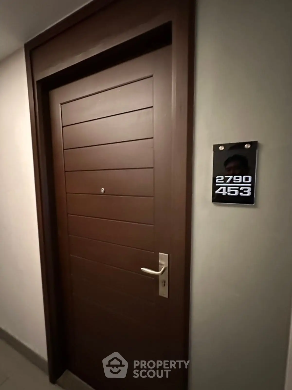 Modern apartment entrance with sleek wooden door and room number plaque.