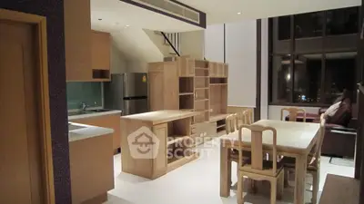 Spacious modern living room with open kitchen and dining area, featuring wooden furniture and large windows.