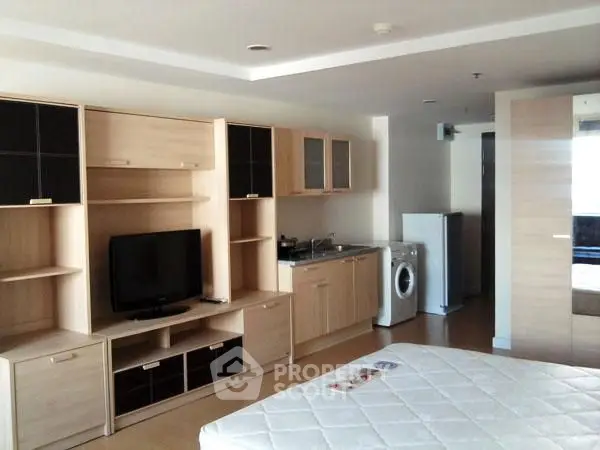 Modern studio apartment with built-in entertainment unit and compact kitchen.