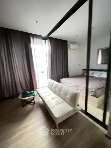 Modern studio apartment with glass partition, cozy bed, and stylish sofa in a well-lit room.