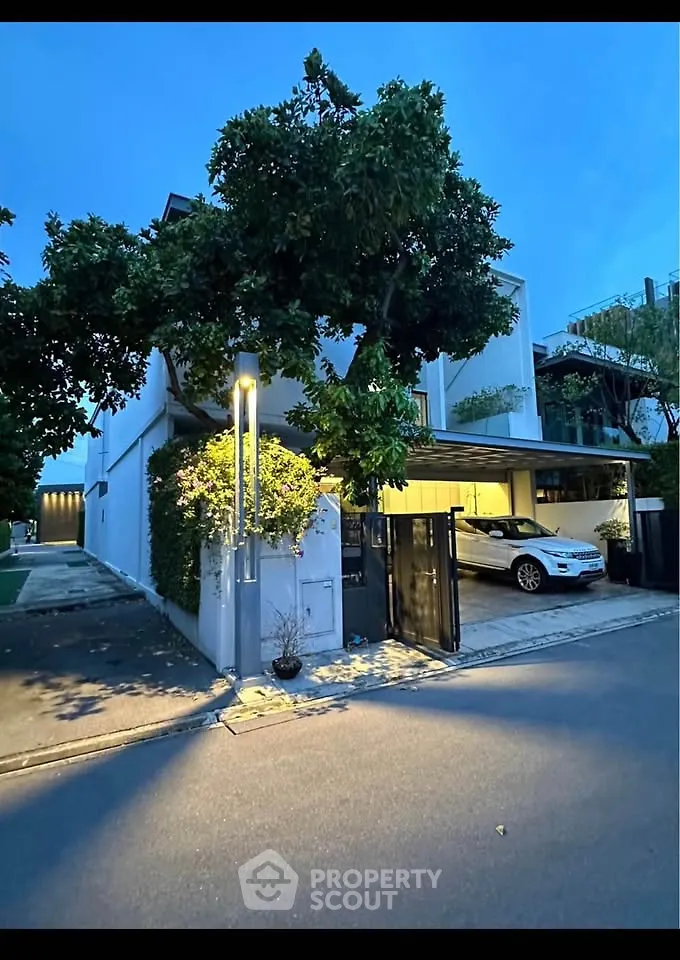 Modern two-story house with carport and lush greenery in a serene neighborhood.