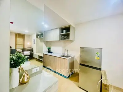 Modern kitchen with stainless steel fridge and cozy living area in open layout apartment.