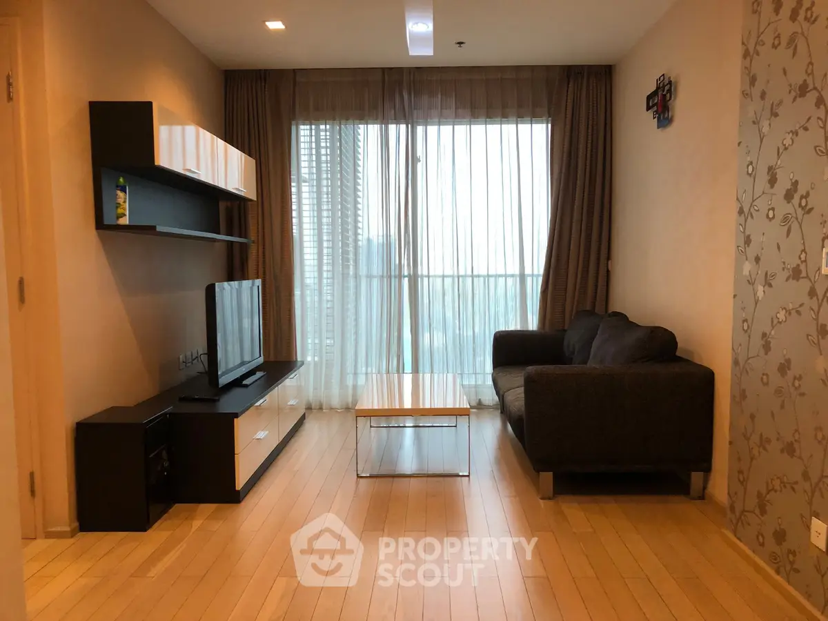 Modern living room with sleek furniture and large window offering city view.