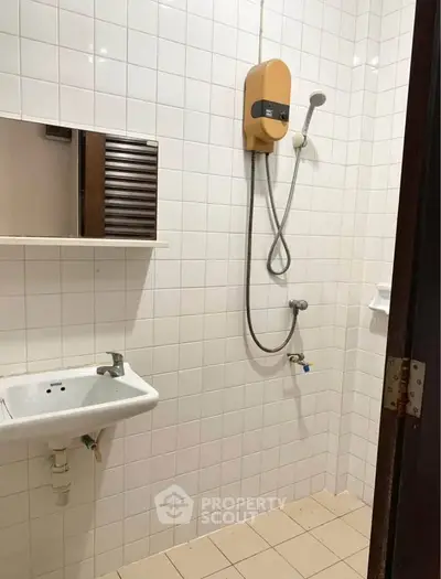 Compact bathroom with wall-mounted shower and sink, ideal for efficient space use.