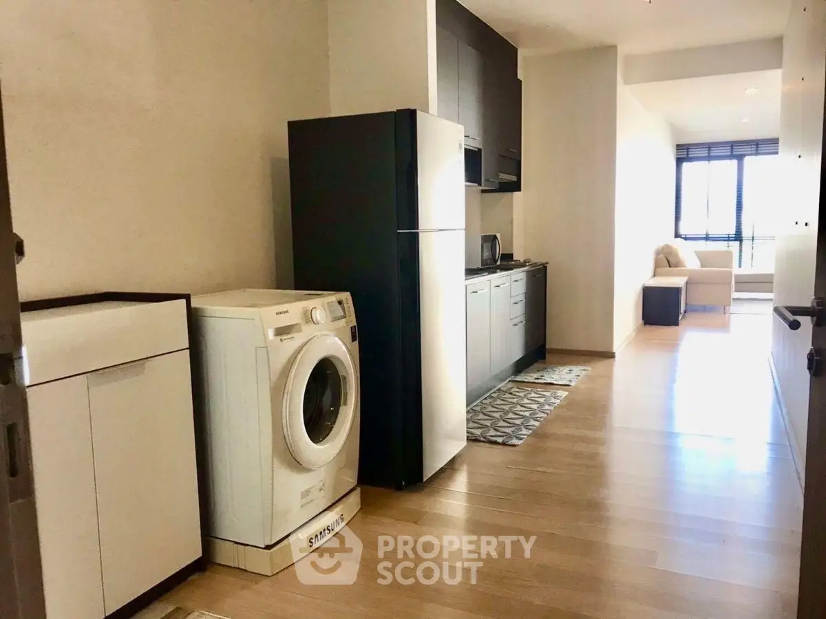 Modern apartment with sleek kitchen and washing machine, featuring bright natural light and cozy living area.