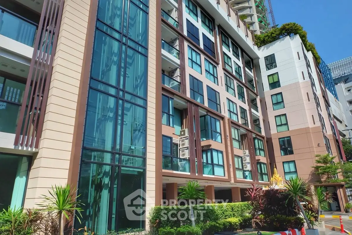 Modern apartment building exterior with lush greenery and large windows in urban setting.