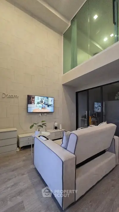 Modern living room with high ceiling and mezzanine, featuring sleek furniture and a wall-mounted TV.