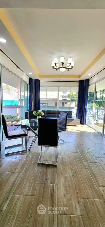 Spacious modern living room with elegant chandelier and large windows offering natural light.