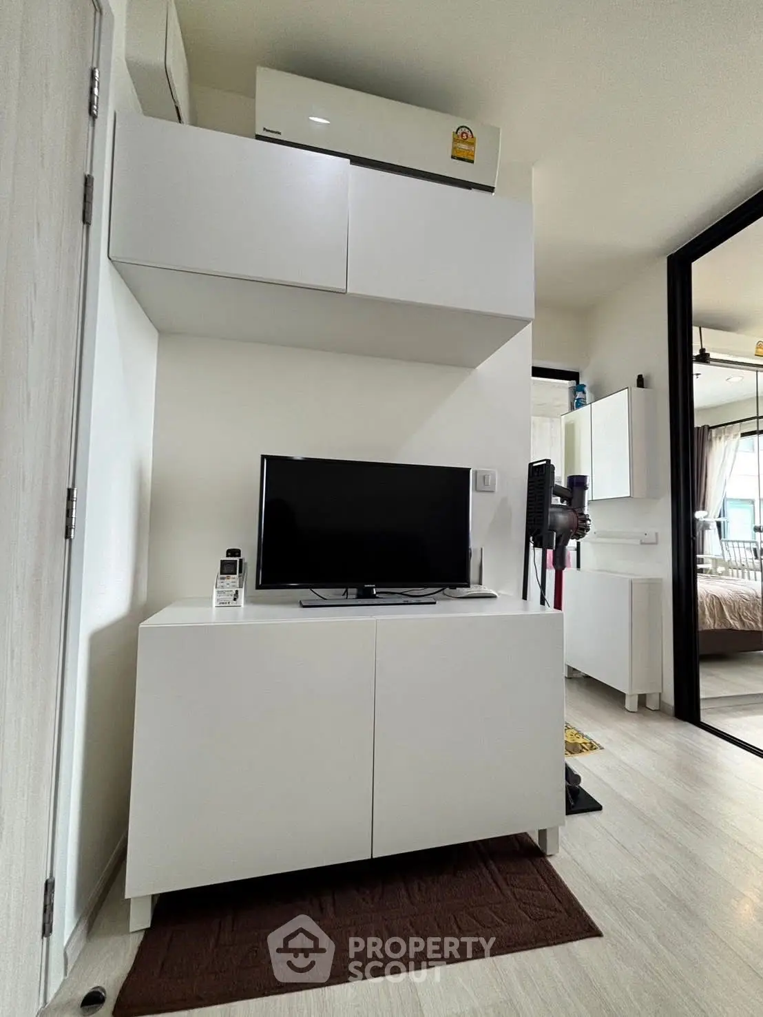 Modern living room with sleek white furniture and TV, showcasing minimalist design and cozy ambiance.