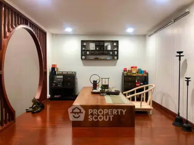 Elegant living room with Asian-inspired decor and wooden flooring, featuring a cozy seating area and unique circular partition.
