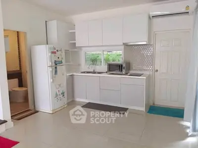 Modern kitchen with sleek white cabinets and appliances, adjacent to a bathroom, in a bright open space.