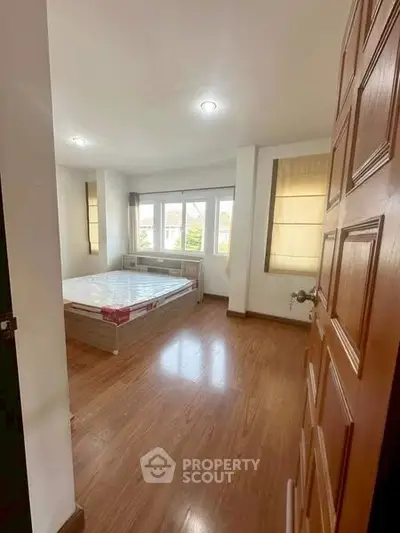 Spacious bedroom with wooden flooring and large windows for natural light.