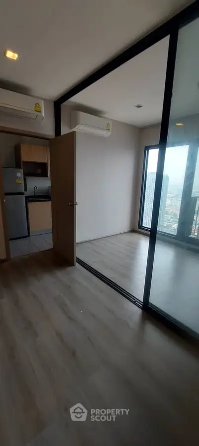 Modern apartment with glass partition and city view, featuring a compact kitchen and sleek flooring.