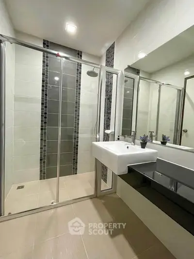 Modern bathroom with glass shower enclosure and sleek vanity in a contemporary home.