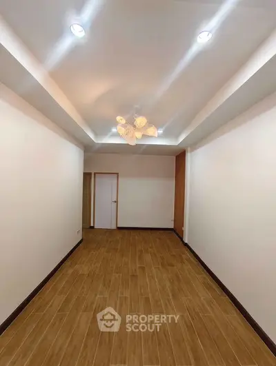 Spacious empty room with wooden flooring and modern ceiling lights, perfect for customization.