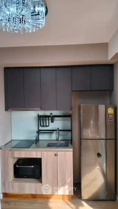 Modern compact kitchen with stainless steel fridge and elegant lighting