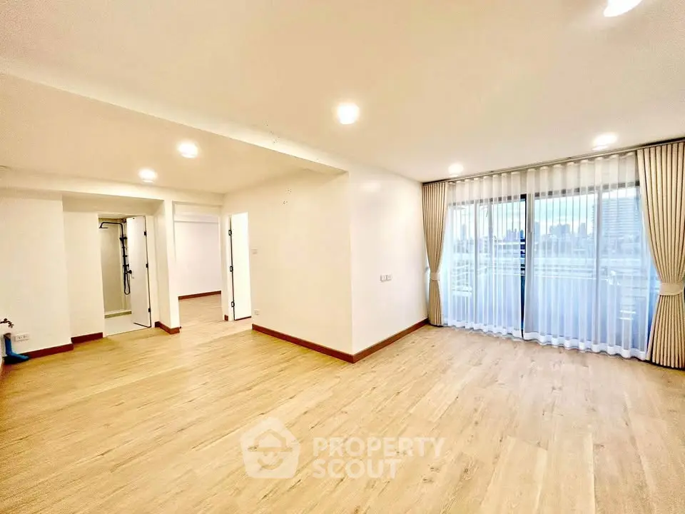 Spacious modern living room with large windows and wooden flooring in a bright apartment.