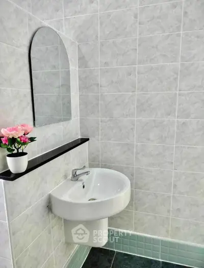 Modern bathroom with sleek sink and elegant wall tiles, featuring a decorative flower arrangement.