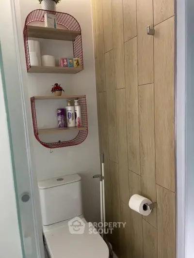 Compact modern bathroom with wall-mounted shelves, wooden door, and white ceramic fixtures for space-efficient urban living.