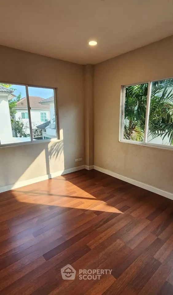 Bright empty room with hardwood floors and large windows offering a garden view.