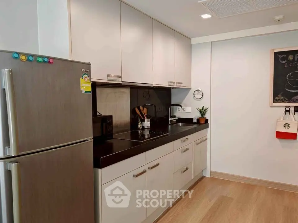 Modern kitchen with sleek cabinetry and stainless steel fridge in a cozy apartment.