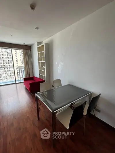 Modern living room with red sofa and dining table, featuring large windows and wooden flooring.