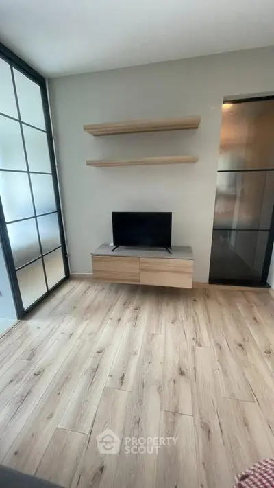 Modern living room with wooden flooring, TV unit, and glass sliding doors.