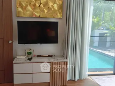 Modern living room with TV, elegant decor, and poolside view through large glass doors.