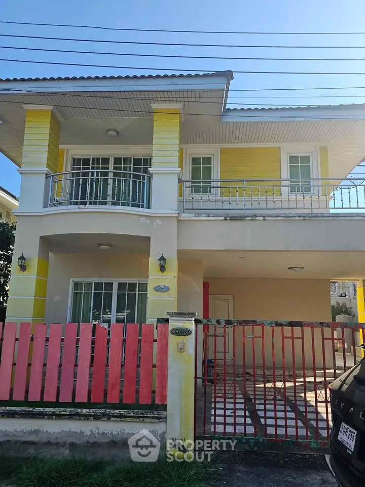 Charming two-story yellow house with balcony and gated entrance, perfect for family living.