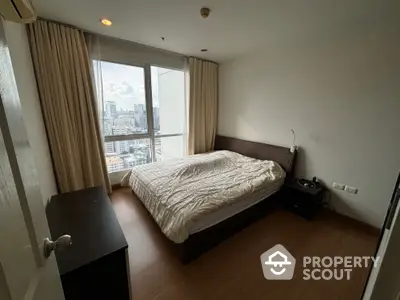 Cozy bedroom with city view, featuring a large window and modern furnishings.