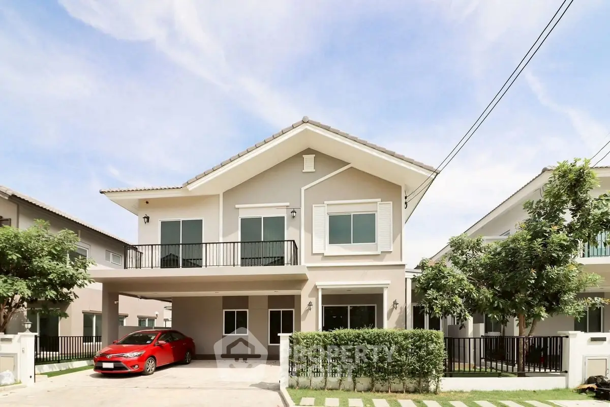 Modern two-story house with a red car parked in the driveway, featuring a spacious balcony and lush greenery.