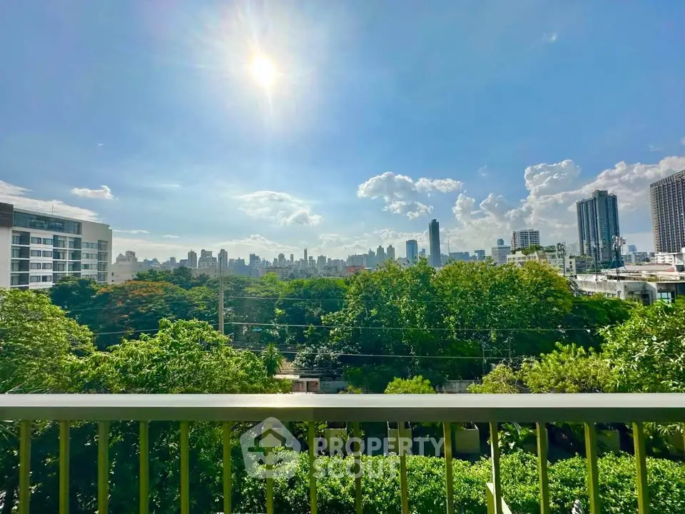 Stunning cityscape view from a balcony overlooking lush greenery and skyline under a bright sun.