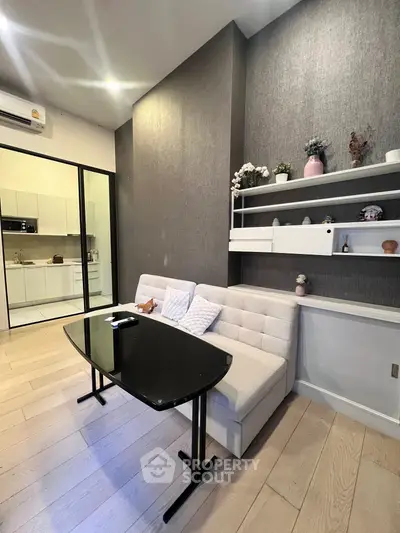 Modern living room with stylish decor and open kitchen layout, featuring sleek furniture and elegant shelving.