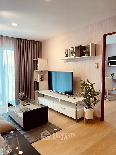 Modern living room with stylish decor and large TV, featuring elegant shelving and natural light.