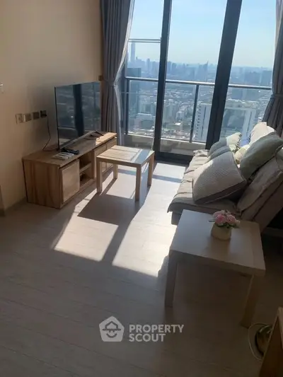 Bright living room with city view, modern furniture, and large windows in high-rise apartment.