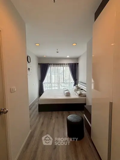 Modern bedroom with city view, featuring sleek furniture and elegant curtains.