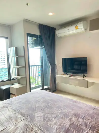 Modern bedroom with balcony view, air conditioning, and sleek TV setup in urban apartment.