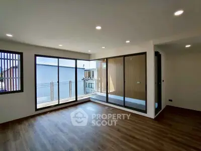 Spacious modern living room with large windows and balcony access, featuring sleek wooden flooring.