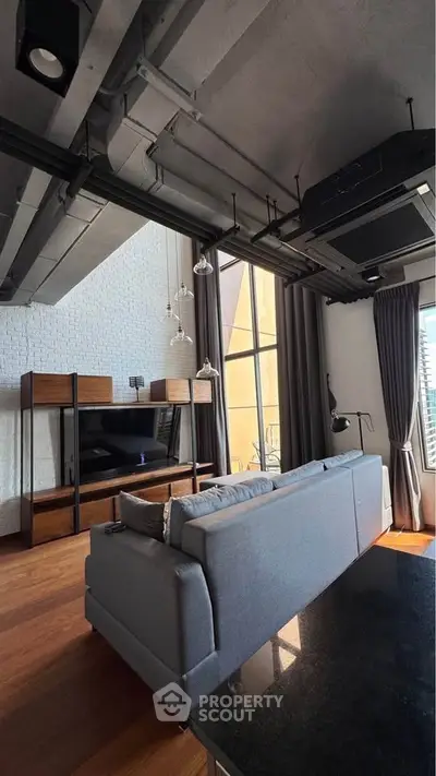 Modern loft living room with high ceilings and large windows, featuring stylish furniture and industrial design.