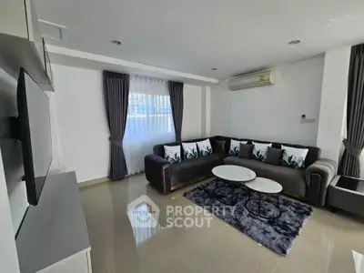 Modern living room with sleek grey sofa, stylish decor, and natural light from large window.
