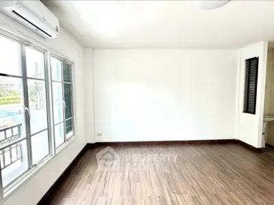 Spacious empty room with wooden flooring and large windows, perfect for customization.