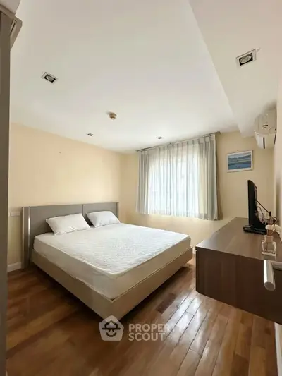 Spacious bedroom with wooden flooring and natural light, featuring a comfortable bed and modern decor.