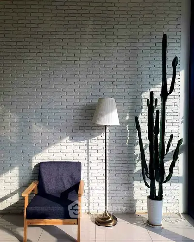 Stylish modern interior with chair, lamp, and cactus against a textured brick wall.