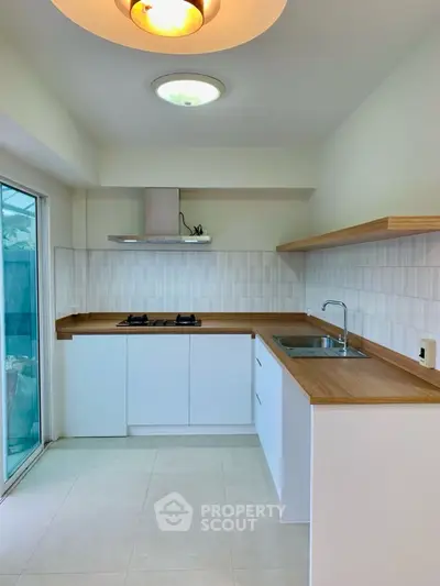 Modern kitchen with sleek white cabinets and wooden countertops, featuring a gas stove and ample natural light.