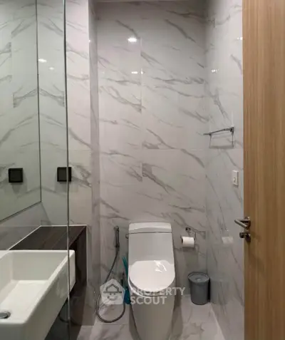Modern bathroom with sleek design and marble tiles, featuring a toilet and a stylish sink.