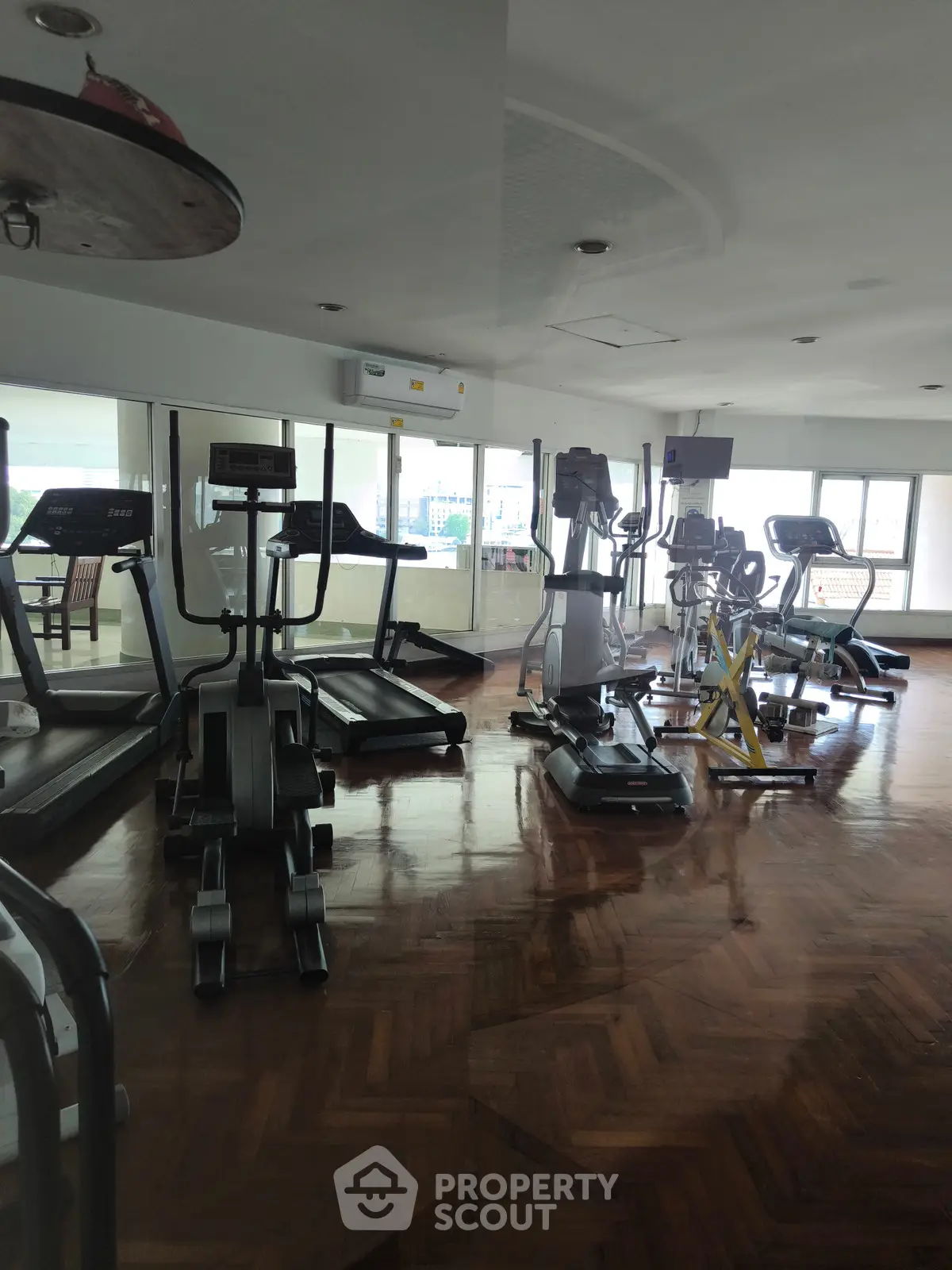 Spacious gym with modern exercise equipment and wooden flooring in a well-lit area.